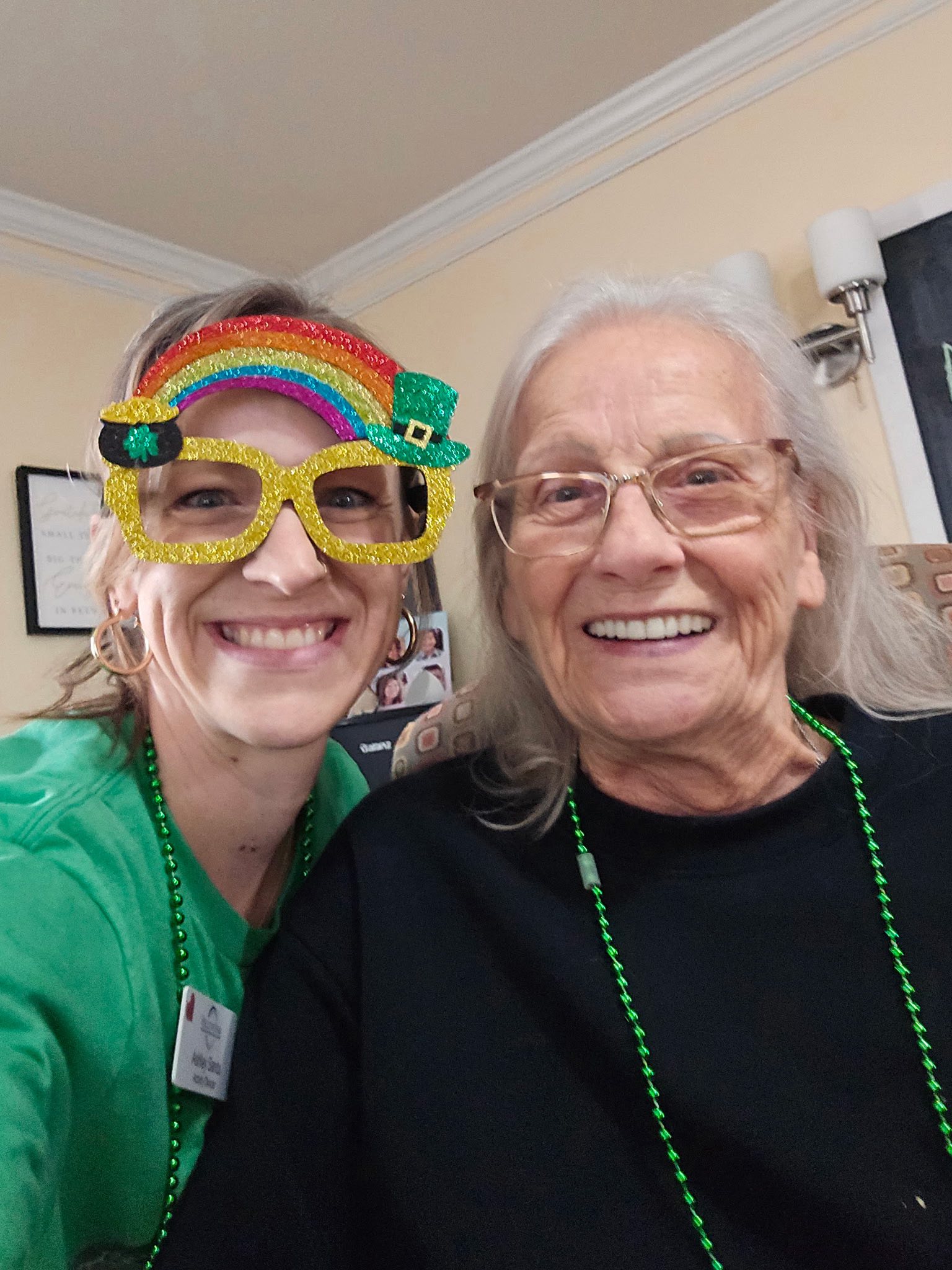 older woman resident at a nursing home in Weatherford, TX with a staff member in St. Patrick's Day glasses